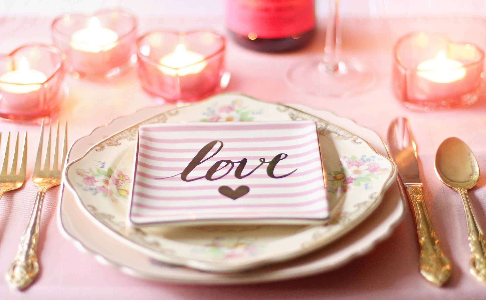 A table setting for Valentine's Day with gold crockery and floral plates. There is a pink and white plate with "Love" written on it with a heart.