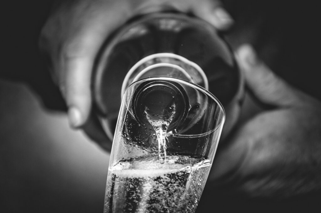 A black and white image of a prosecco or champagne bottle pouring into a glass