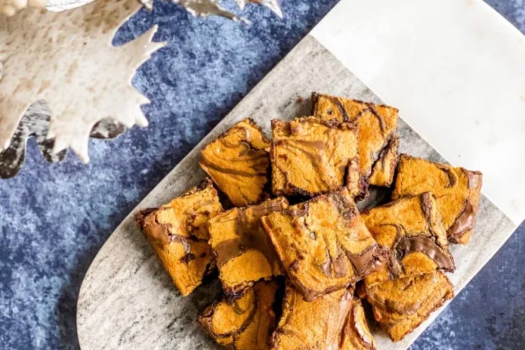 Pumpkin and chocolate swirled brownies on a wooden board, sitting on a blue background
