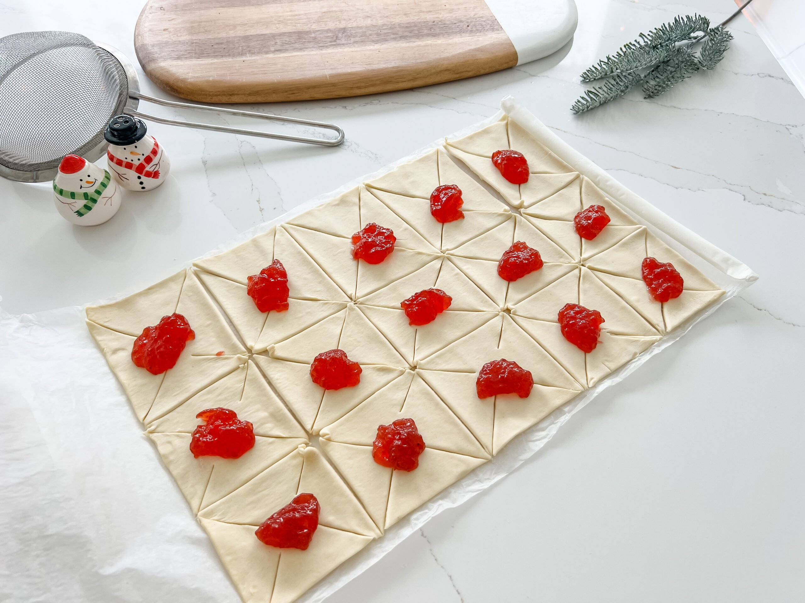 A pre-rolled puff pastry sheet cut into squares and then with cuts in the diagonal of each corner, and a spoonful of jam in the middle of each one