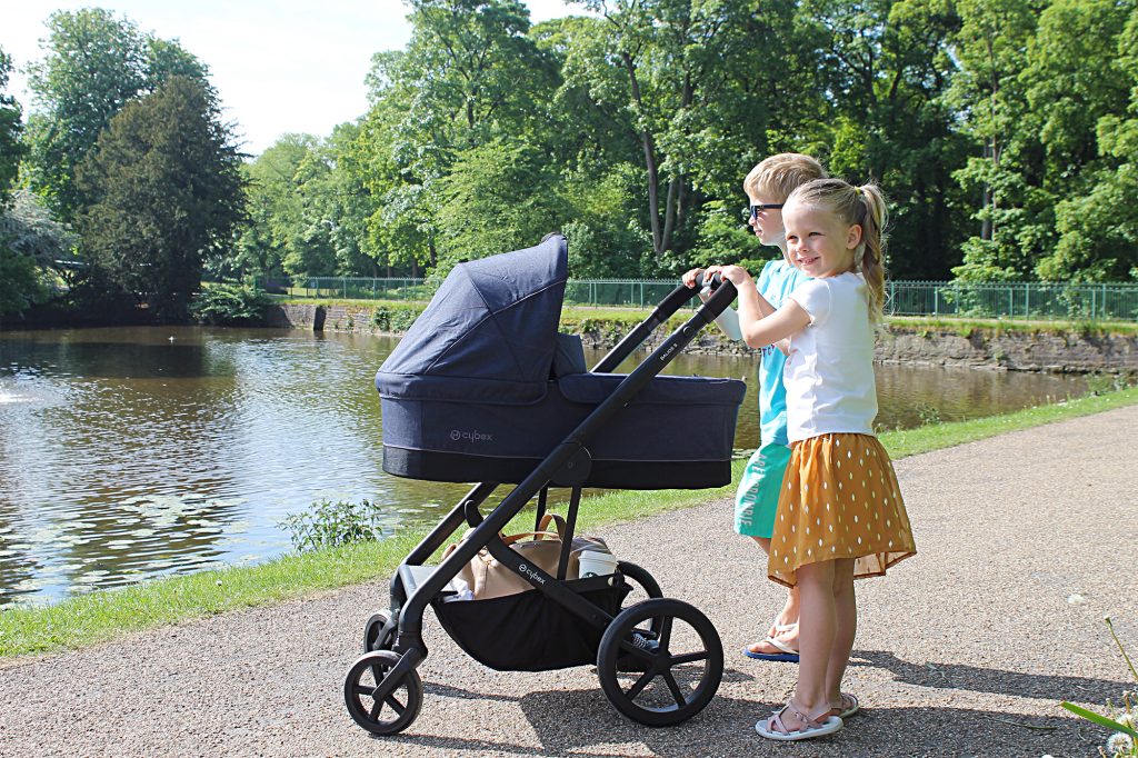 A young girl and boy standing with a Cybex Balios S 3-in-1 Travel System next to a lake