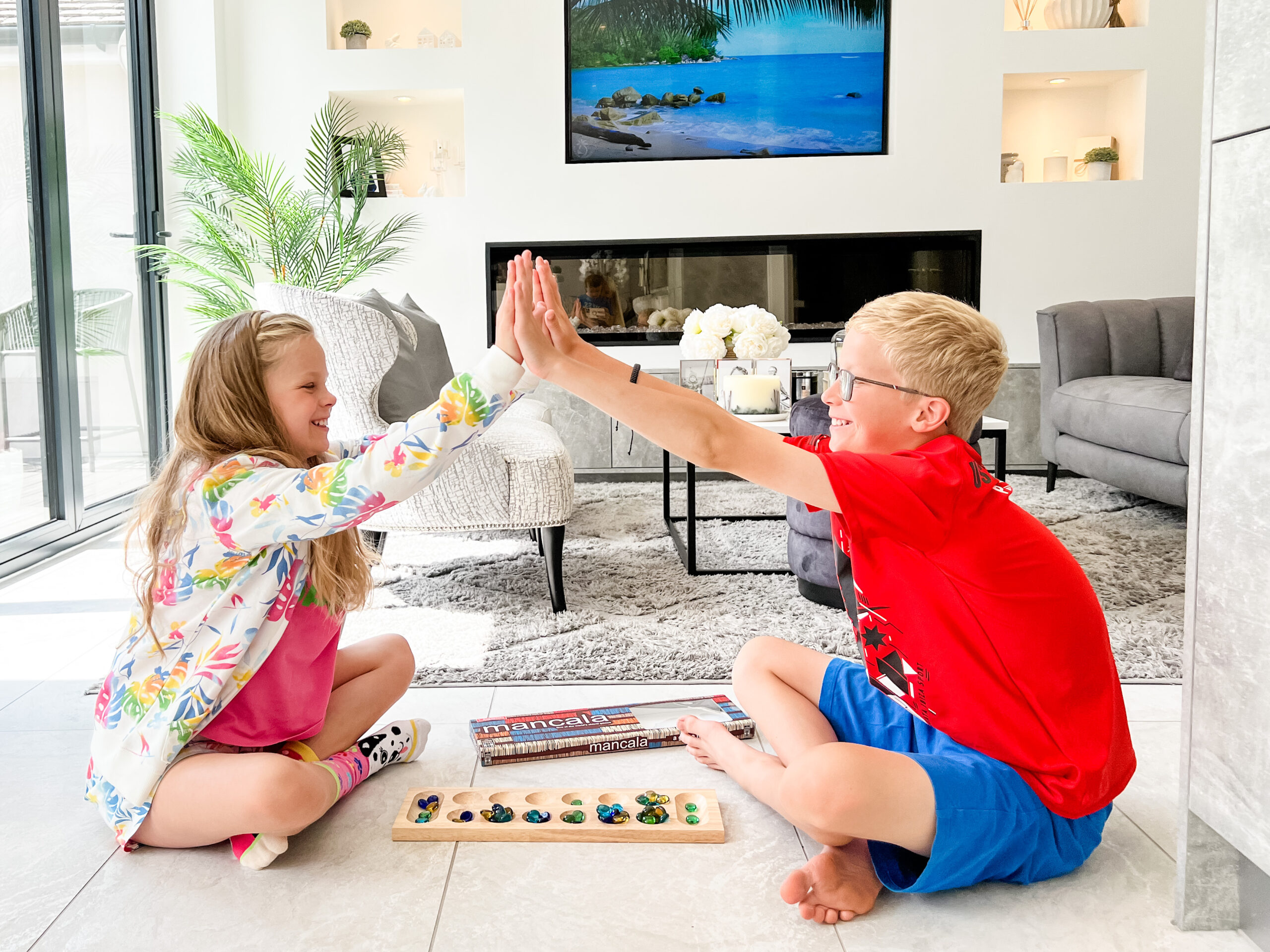 2 children sit on the floor playing a game. They give a double high five above the game