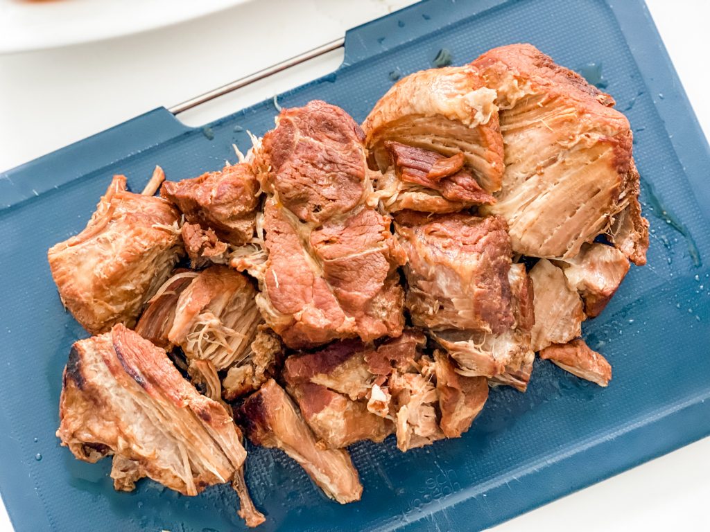 Some slow cooked pork on a blue chopping board before it is shredded