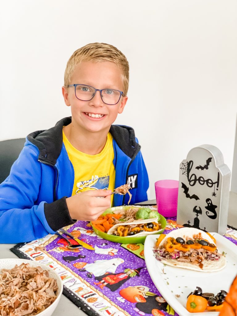 A boy smoking and eating pulled pork at a table decorated for Halloween