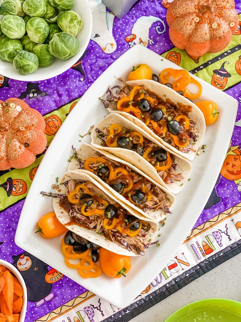 A top down view of some pulled pork tacos, garnised with orange peppers and olives