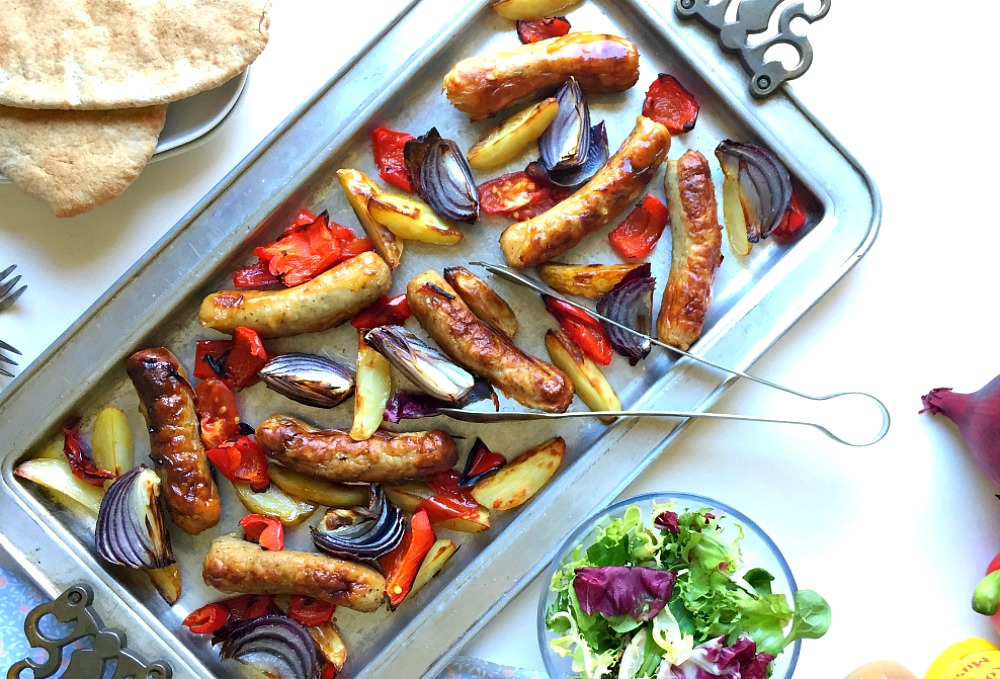 A roasting tray of sausages, peppers and onions