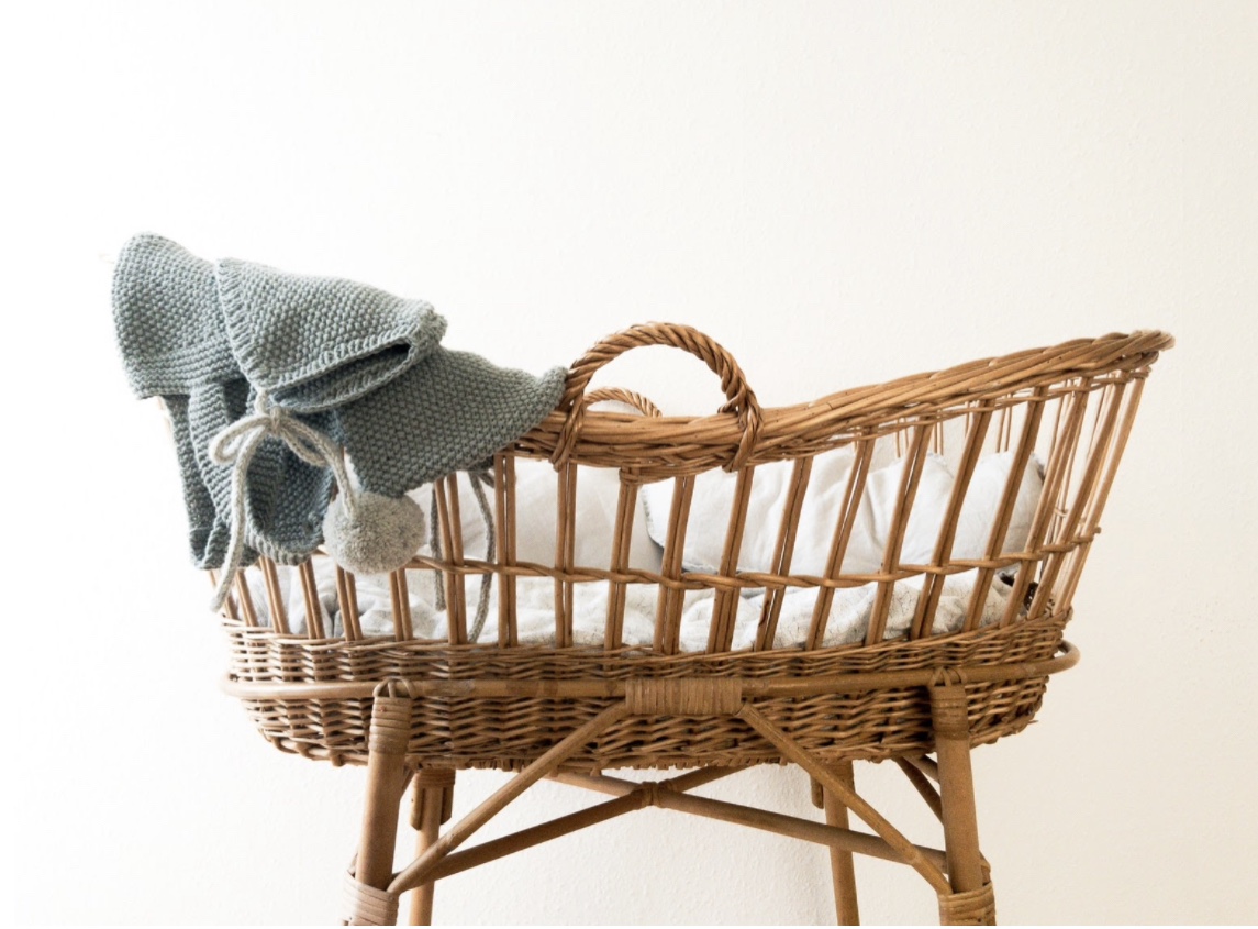 A wicker baby bassinet with a grey blanket draped over the side