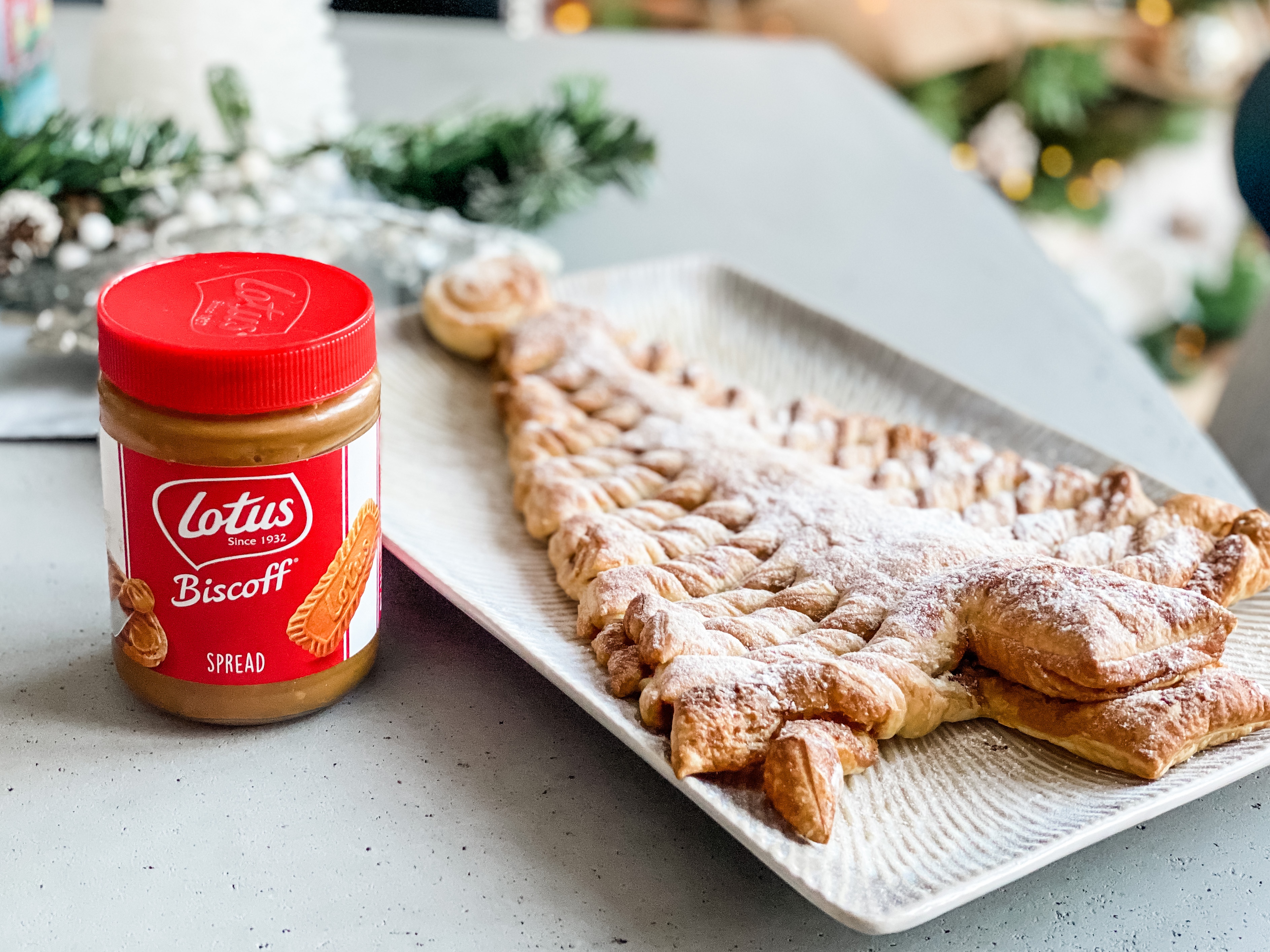 A puff pastry Christmas tree sprinkled with icing sugar. A tub of Lotus Biscoff sits next to it