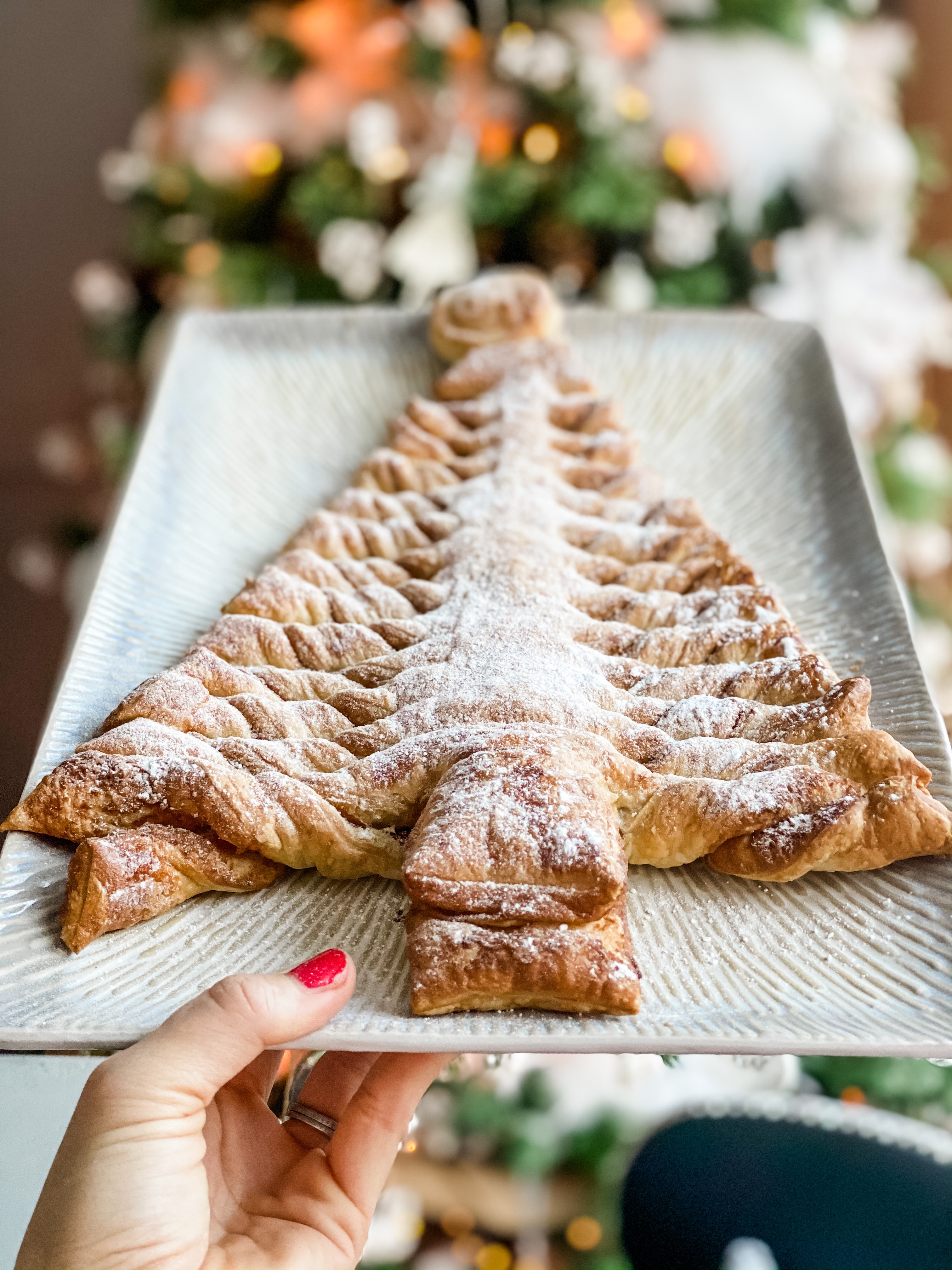 A puff pastry Christmas tree being held in front of a read Christmas tree