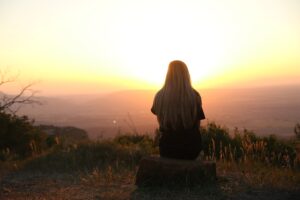 A woman sitting on top of a hill, mesmerized by the breathtaking sunset.