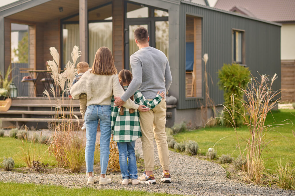 A modern family is standing in front of a small house, showcasing the practicality of tiny homes.
