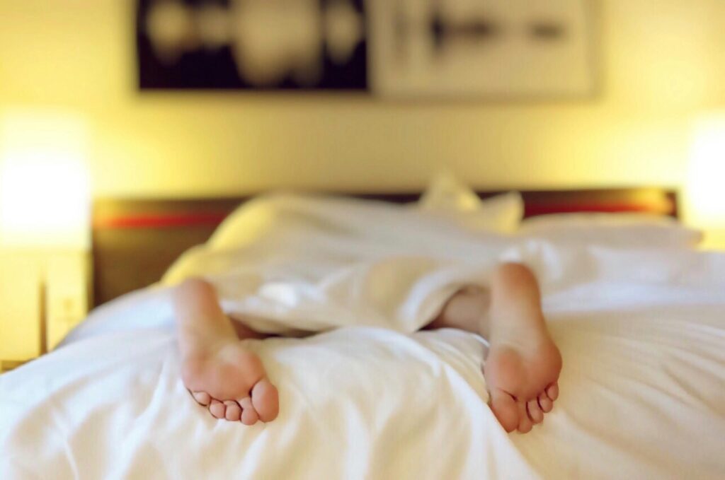 A person's feet are fixing in a bed with white sheets, going through their sleep cycle while feeling depressed.