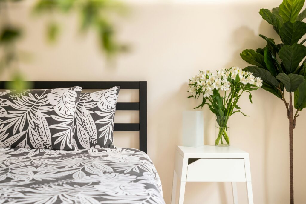 A black and white bedroom with a plant on the side of the bed adorned with flowers.