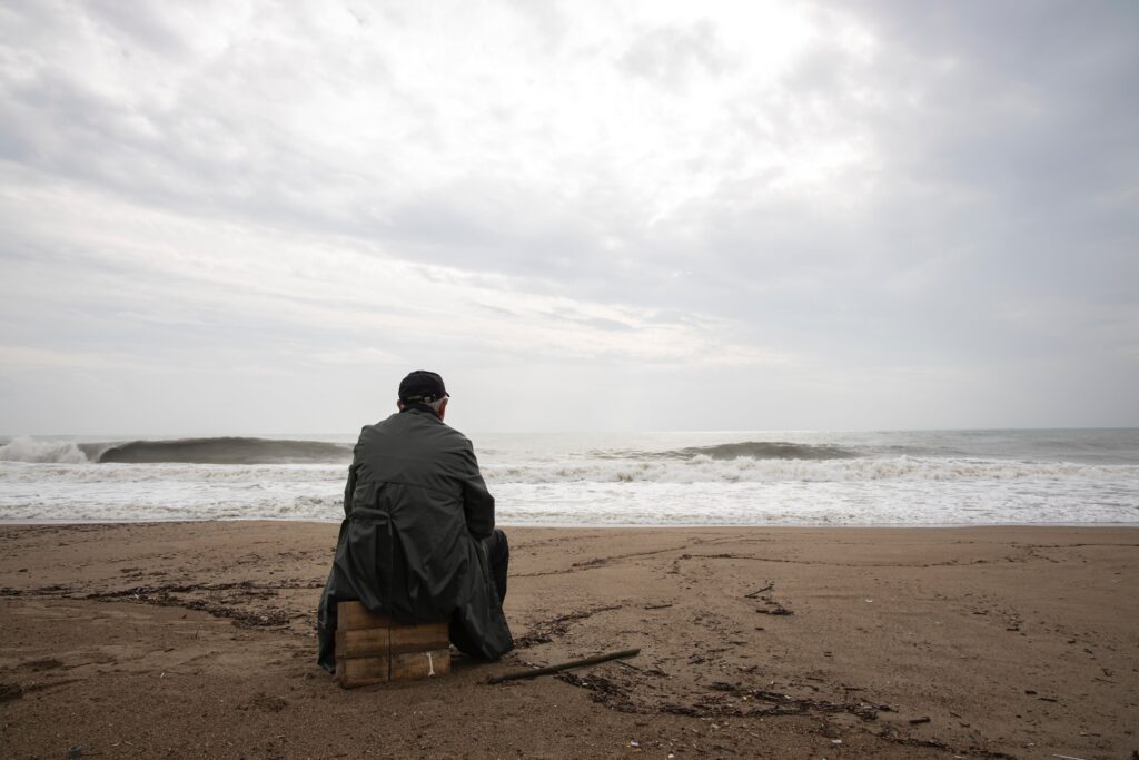 A man sitting on a crate on the beach, contemplating the Pillars of Addiction Treatment.
