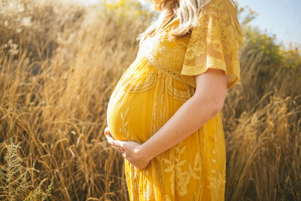 A pregnant woman in a yellow dress gracefully balancing motherhood while standing in a field, prioritizing her prenatal health.