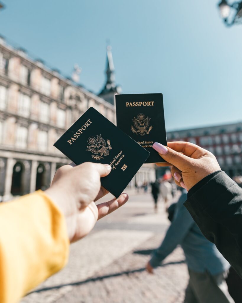 Two people holding passports in front of a building, discussing their EB-2 NIW Visa applications and the US Job Market.