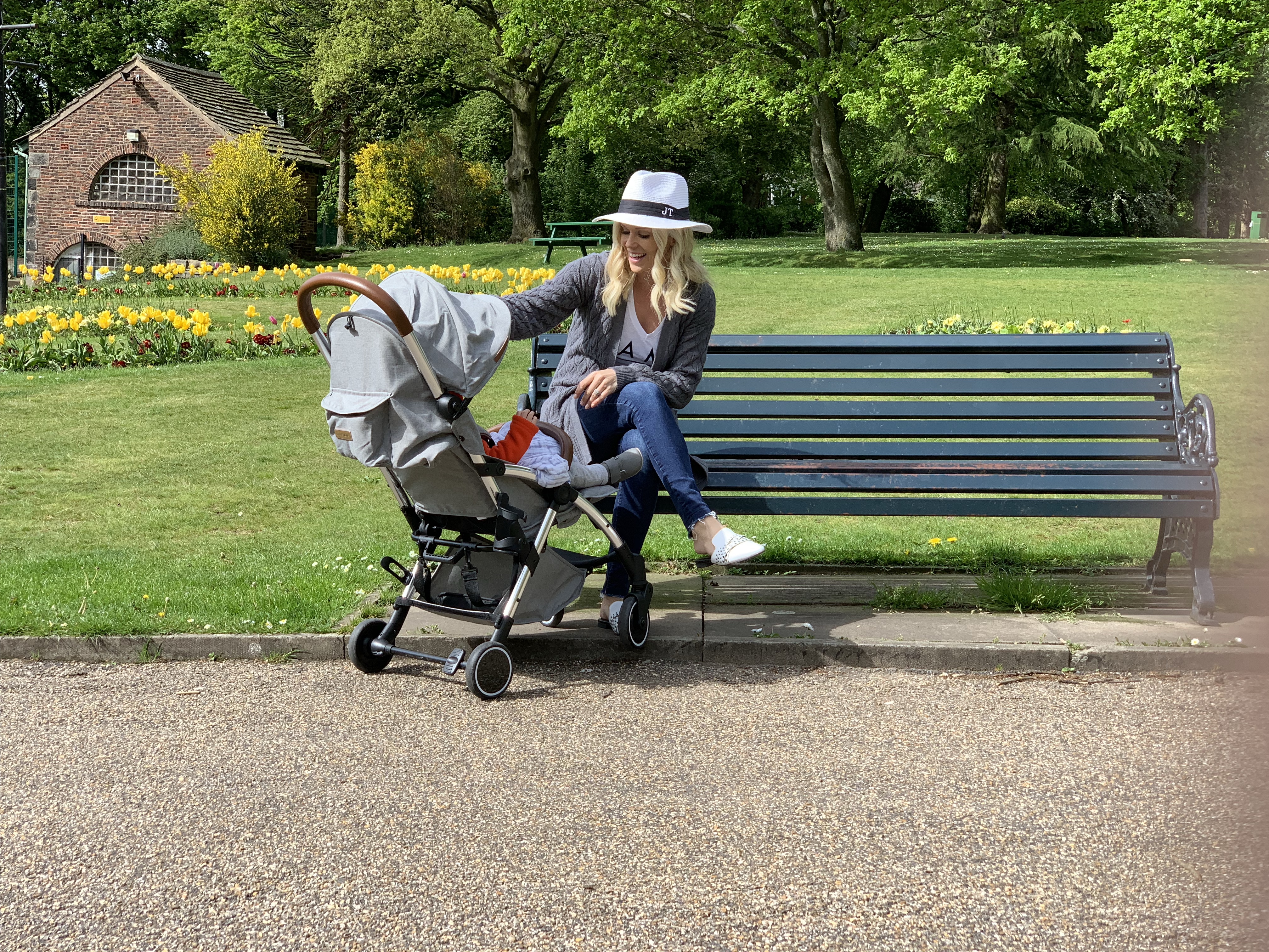 A woman sitting on a park bench, speaking to her baby in a grey stroller