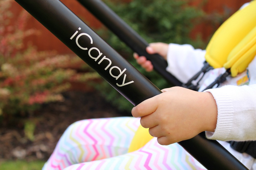 The handle of an iCandy pushchair with a child in the seat holding on