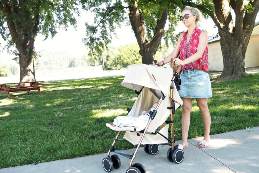 A woman pushing a tan coloured stroller in the park with a young baby in it
