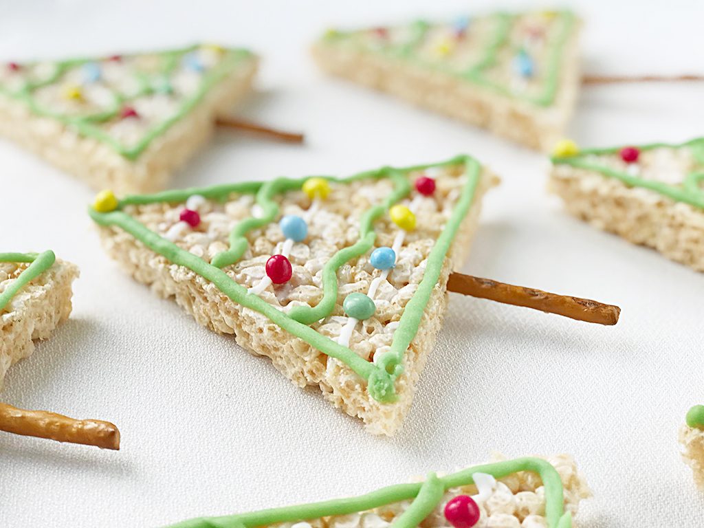 Rice Krispy Treats in triangle shapes like Christmas trees, decorated and with a pretzel stick for a trunk.