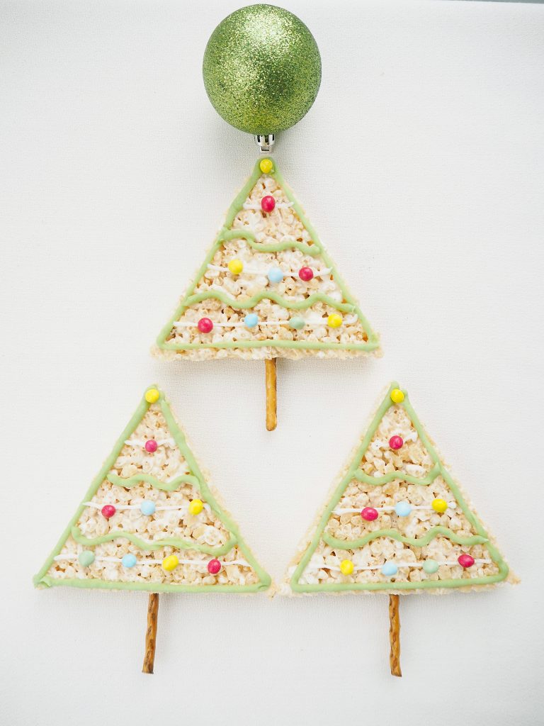 Rice Krispy Treats Christmas Trees with pretzel trunks lines up in a triangle shape like a Chirstmas tree