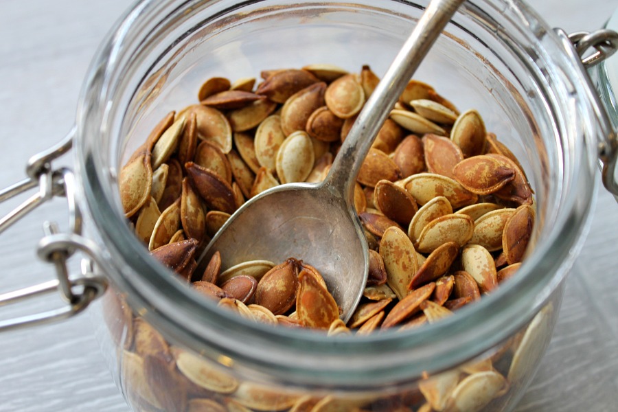 Roasted pumpkin seeds in a glass jar with a spoon sticking out of it