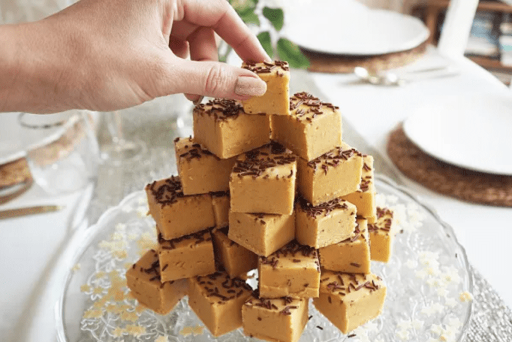Pumpkin Fudge stacked on a glass plate. A hand is reaching out to take the top piece