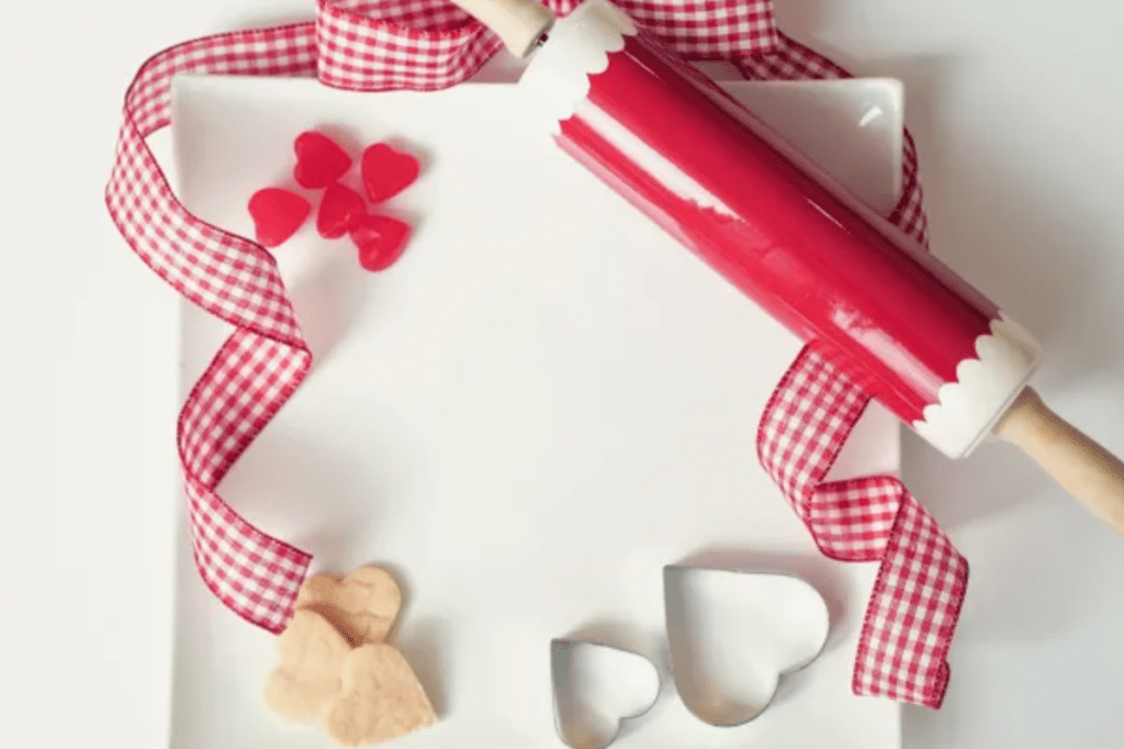 A red rolling pin with heart shaped cookie cutters and gingham ribbon