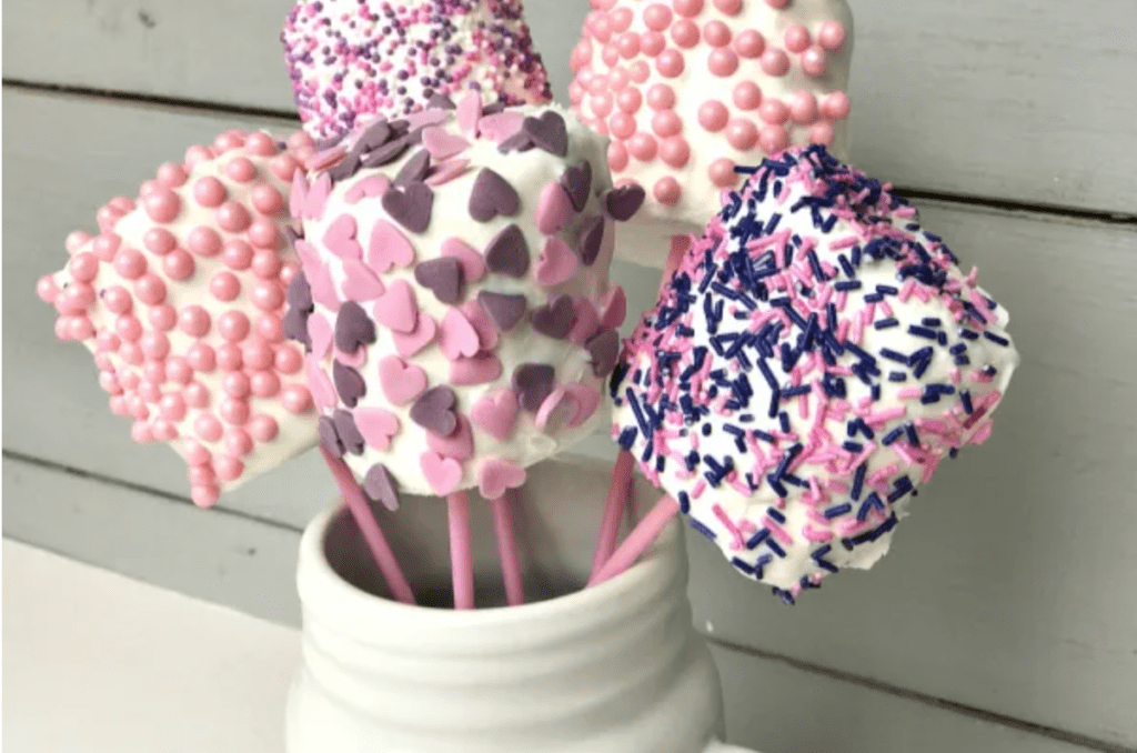 A cream vase filled with with marshmallow pops covered in pink and purple sprinkles