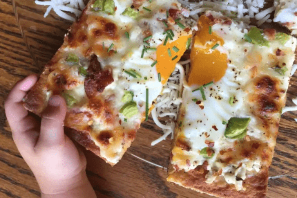A child's hand reaching to take a slice of breakfast pizza with an egg on it