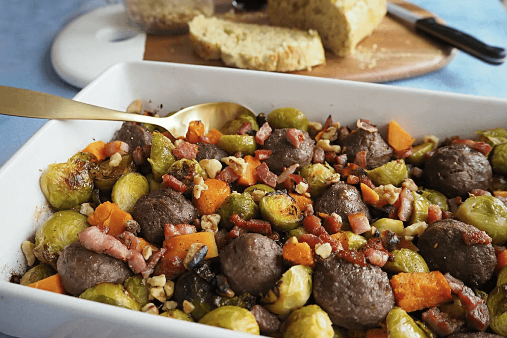 A baking dish filled with meatballs, bacon, brussel sprouts and sweet potato