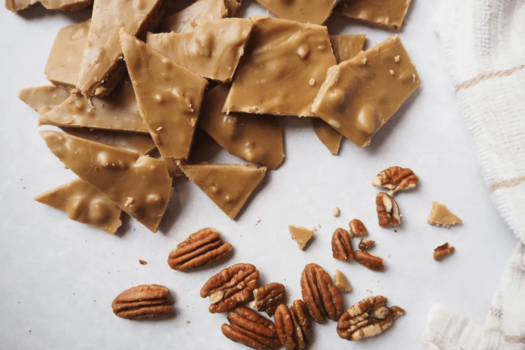 caramel coloured frosting bites broken into shards, next to a small pile of pecans